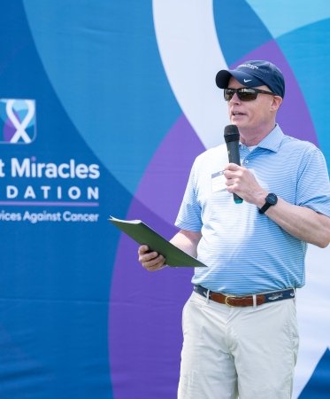 Man speaking into a microphone in front of an Expect Miracles Foundation backdrop