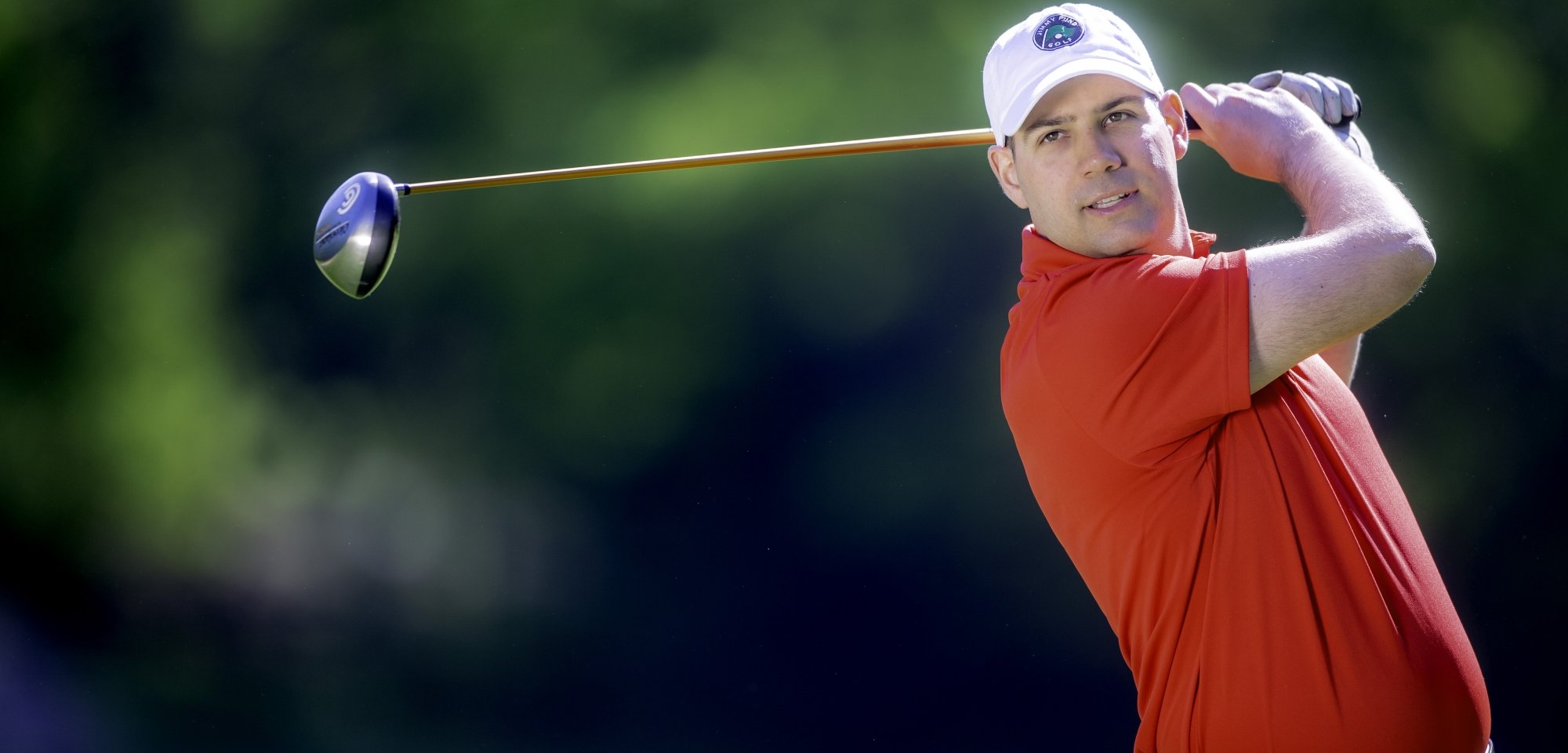 A golfer taking a swing wearing a Jimmy Fund Golf hat