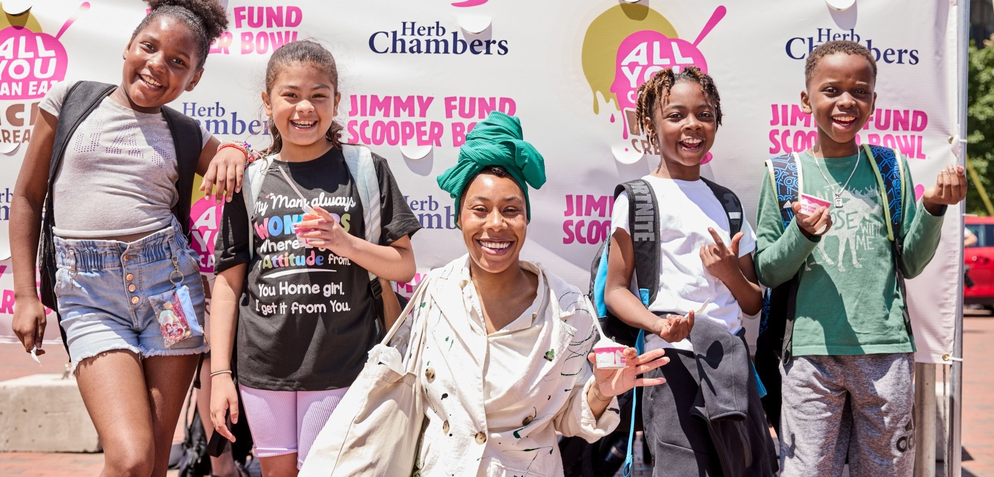 A woman and four children hold ice cream in front of a Jimmy Fund Scooper Bowl backdrop