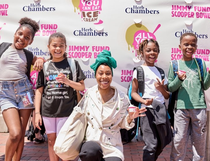 A woman and four children hold ice cream in front of a Jimmy Fund Scooper Bowl backdrop