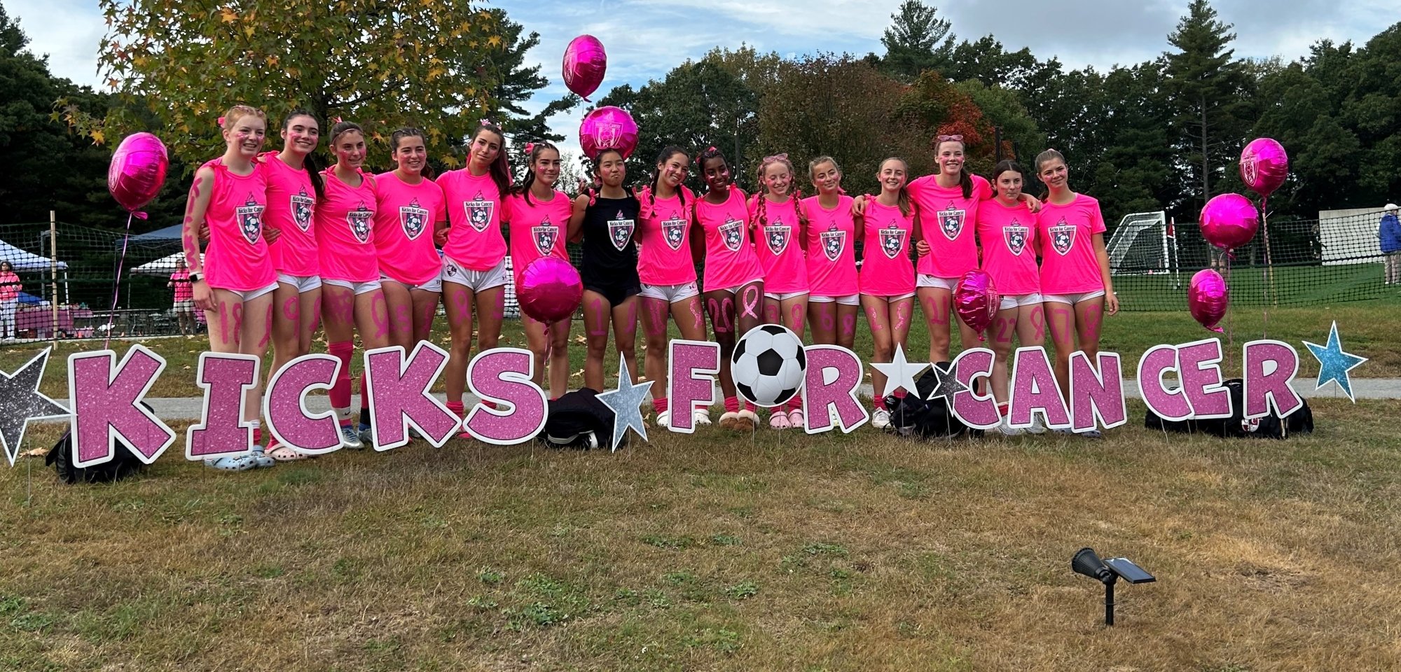 A soccer team poses in front of giant letters spelling Kicks for Cancer
