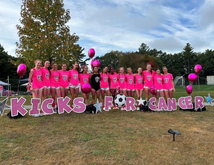 A soccer team poses in front of giant letters spelling Kicks for Cancer