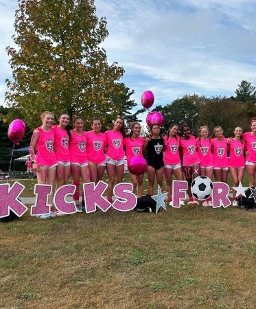 A soccer team poses in front of giant letters spelling Kicks for Cancer