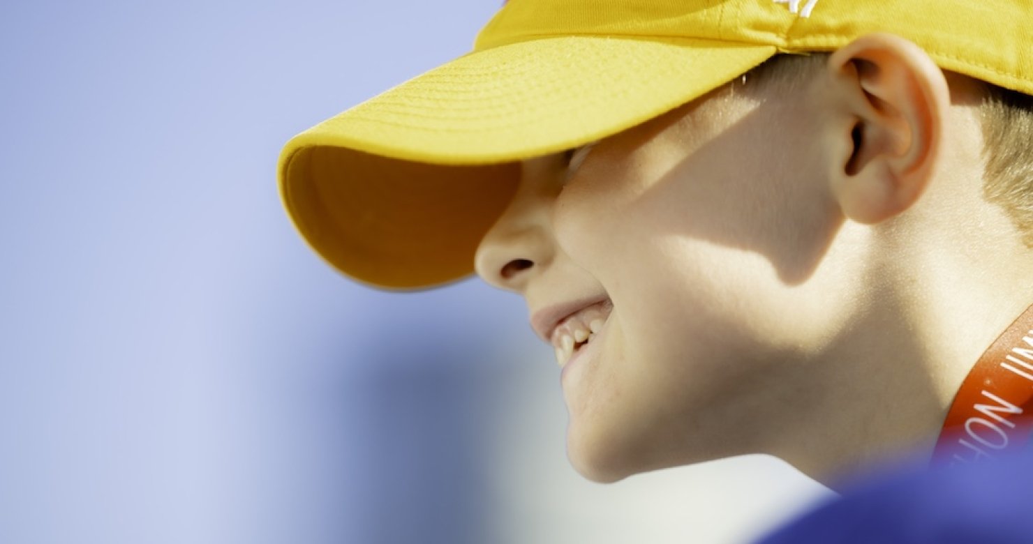 Side profile of a smiling child wearing a yellow ‘47 brand hat