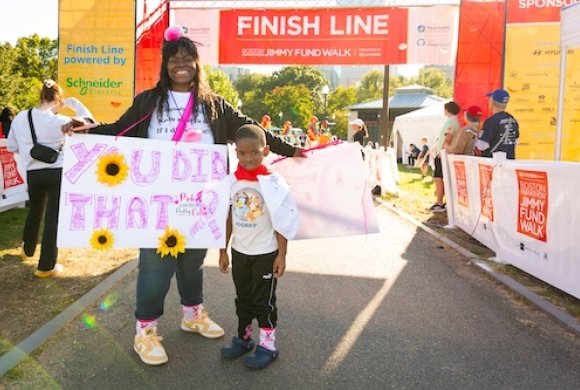 A woman and a young boy at the finish line at the Jimmy Fund Walk holding a poster that says ’You did that’