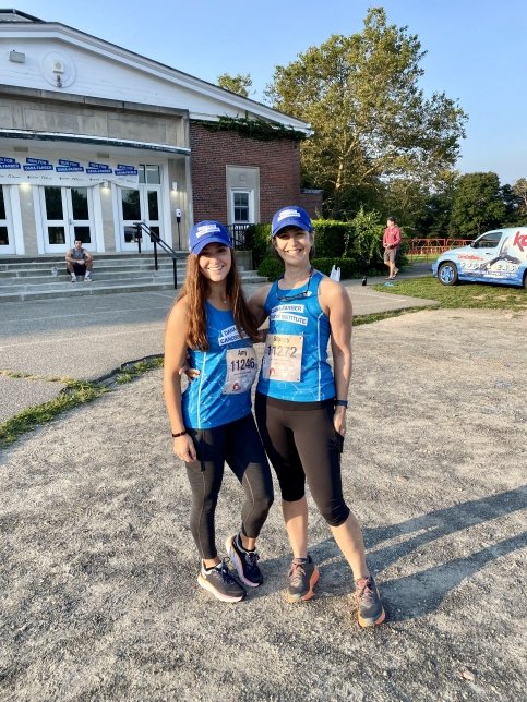 Stacey stands in a parking lot with another runner, both wearing Dana-Farber singlets
