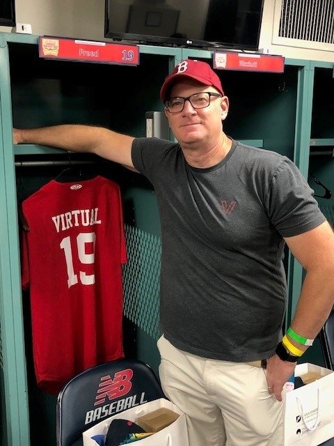 Andy stands in locker room in front of a Red Sox jersey that says 'Virtual' on the back