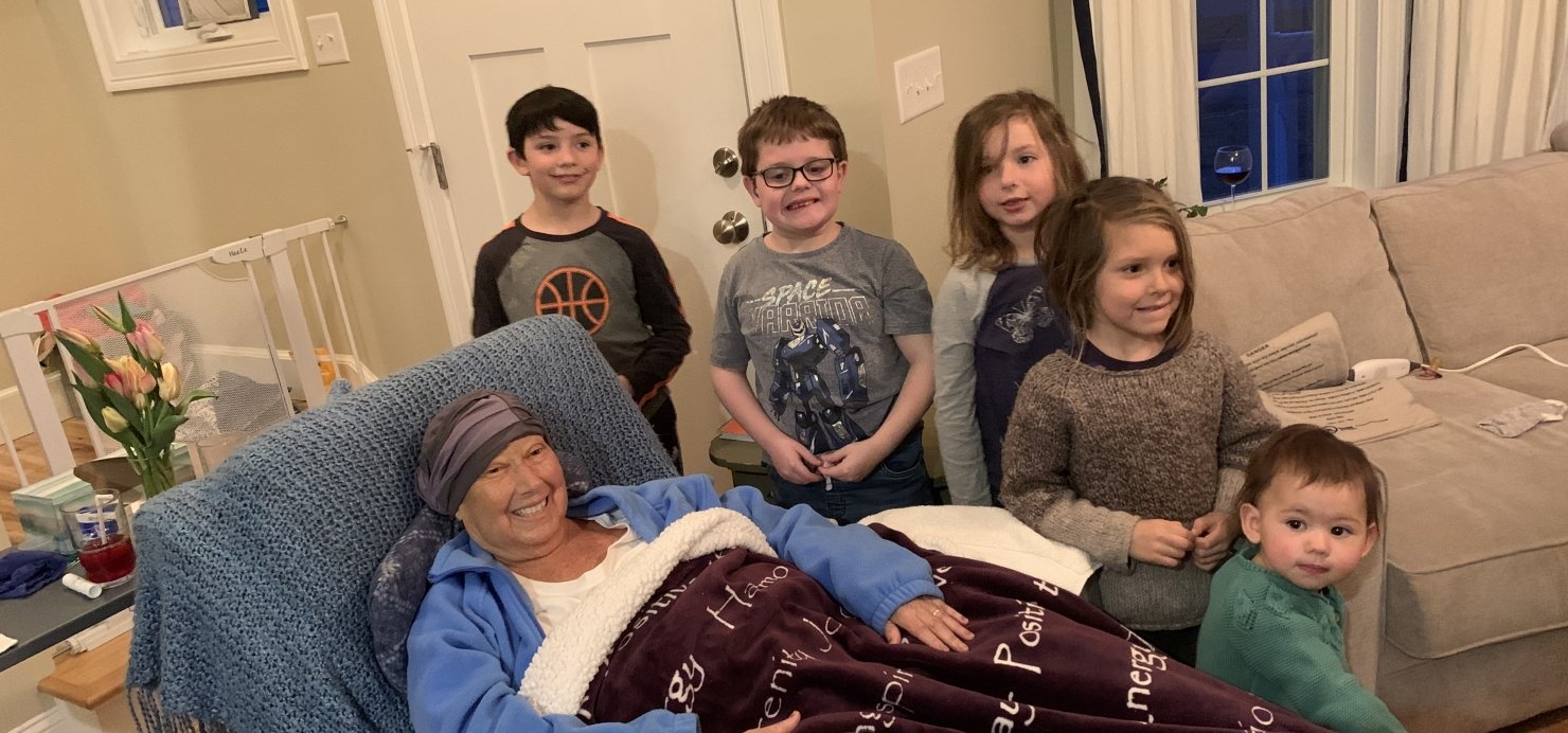 Joanna lies in bed in living room with five young children standing next to her