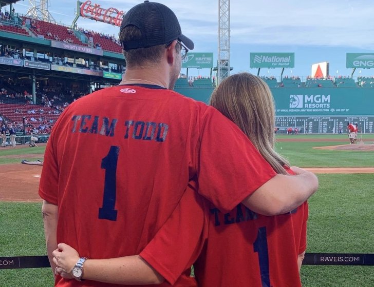 Laura and Adam hug looking out at Fenway Park field