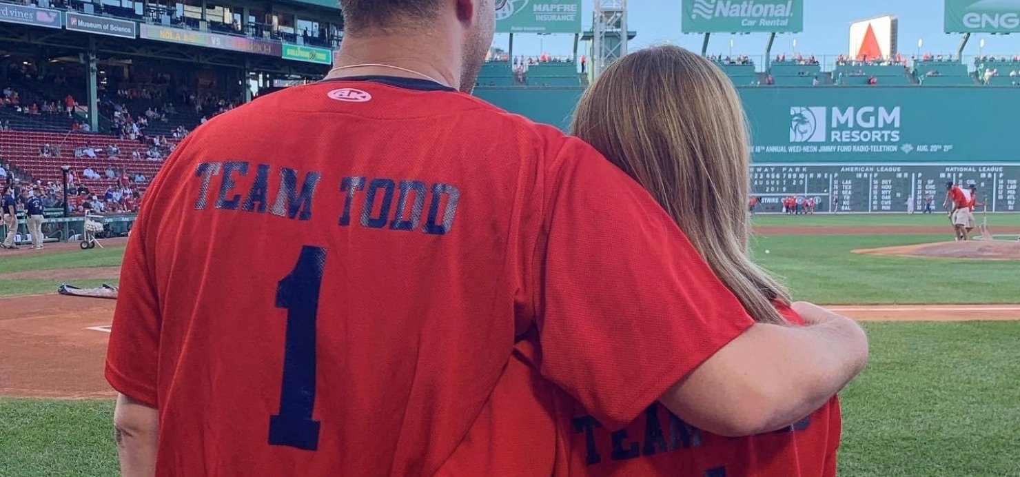 Laura and Adam hug looking out at Fenway Park field