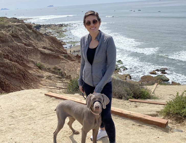 Jenny holds a dog while standing on a beach cliff