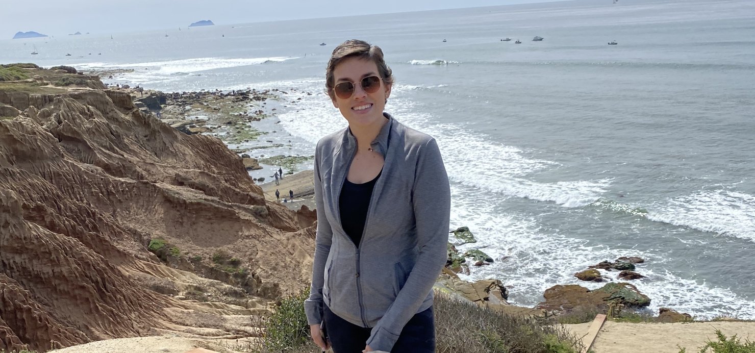 Jenny holds a dog while standing on a beach cliff