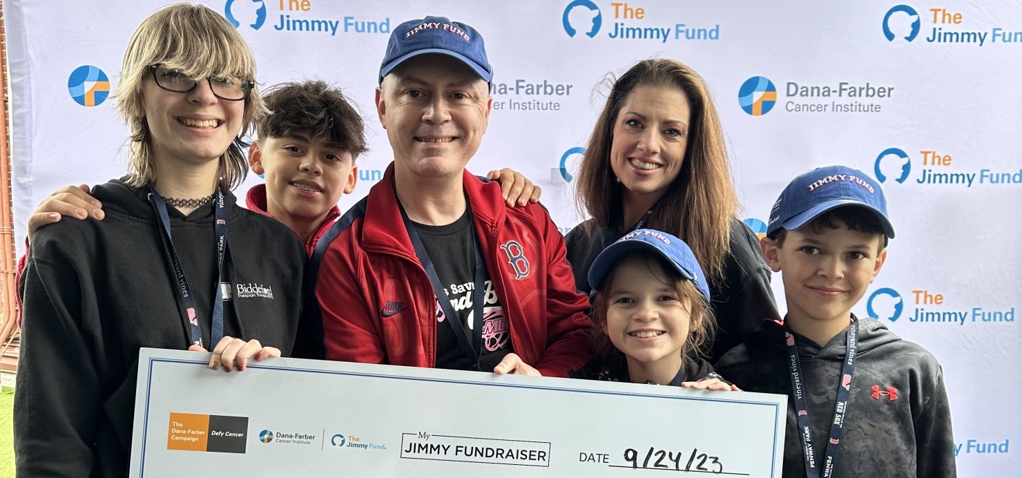 James and family hold a large check in front a Jimmy Fund backdrop