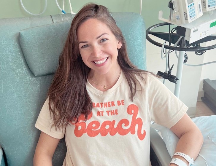 Julie sits in a hospital bed smiling wearing 'I’d rather be at the beach' T-shirt