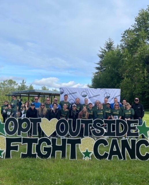 Group stands in field with a sign reading 'Opt Outside, Fight Cancer'