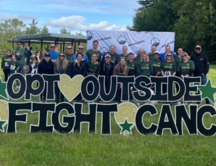 Group stands in field with a sign reading 'Opt Outside, Fight Cancer'