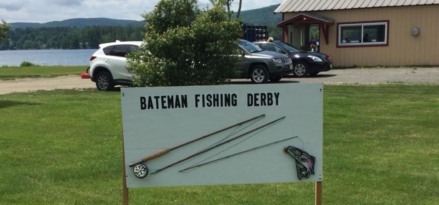 Sign reading 'Bateman Fishing Derby' with a lake and woods in the background