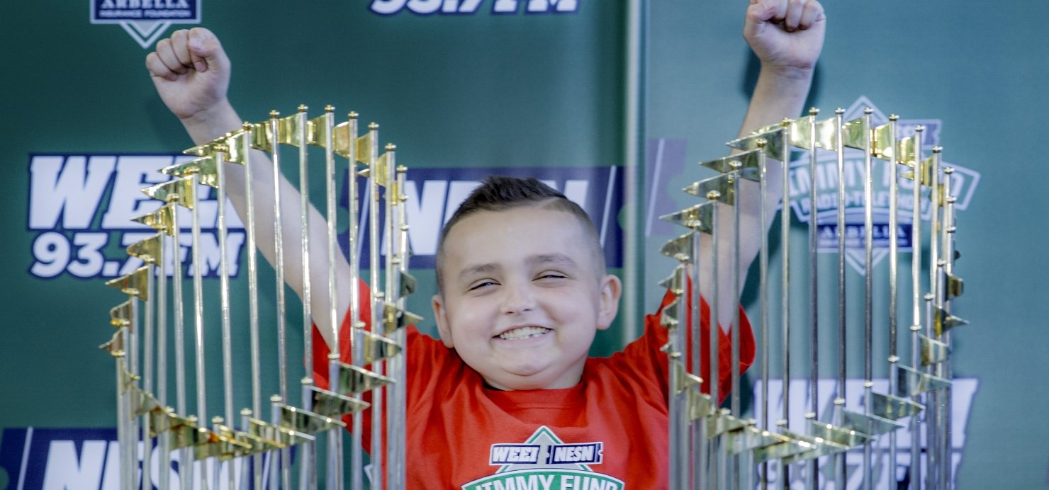 Grady stands with both arms in the air behind two championship trophies