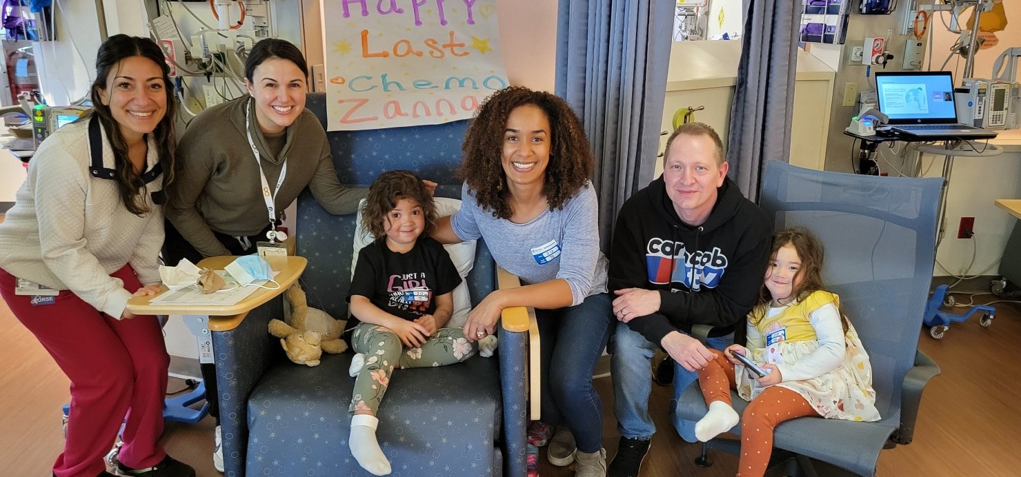 Zanna and family sit in front of a 'Happy Last Chemo, Zanna' sign in the Jimmy Fund clinic