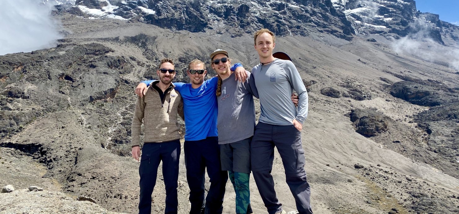 Four friends stand in front of tall mountain