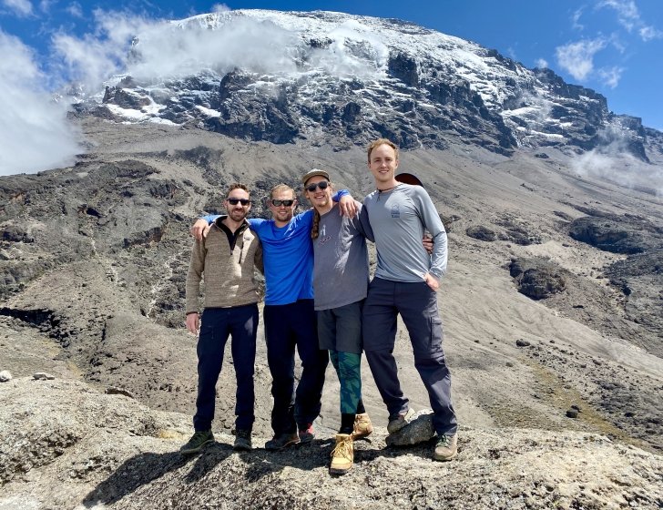 Four friends stand in front of tall mountain