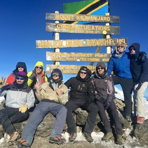 John sitting on Mount Kilimanjaro summit with group of friends