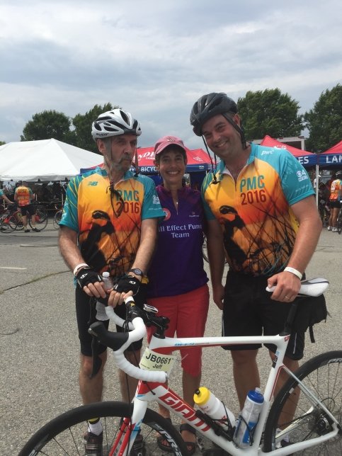 Three riders stand together holding a bike