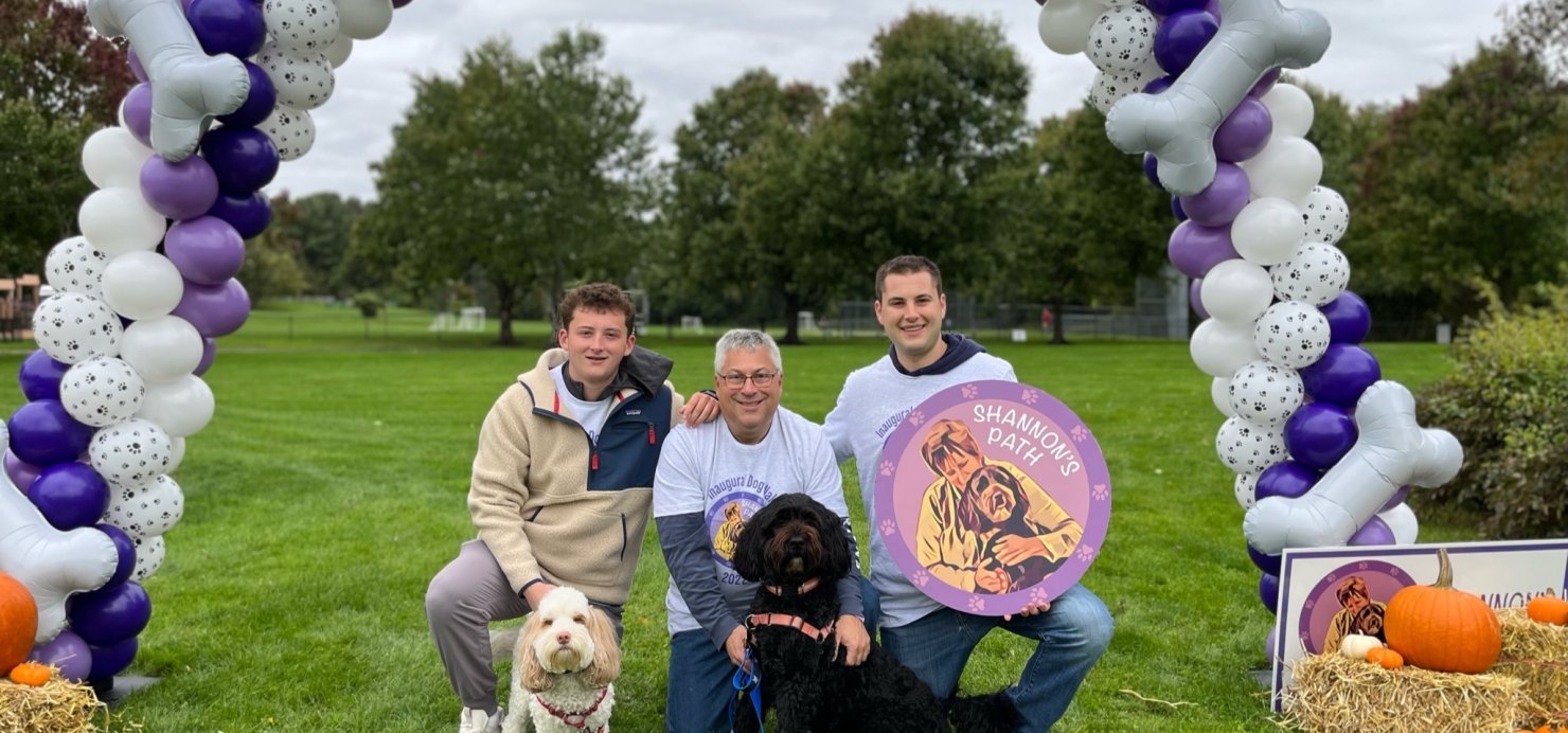 Family and dogs sit in a field under balloon arch