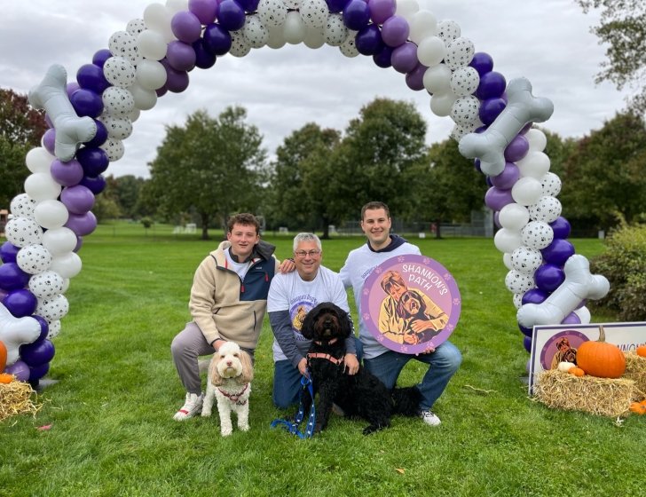 Family and dogs sit in a field under balloon arch