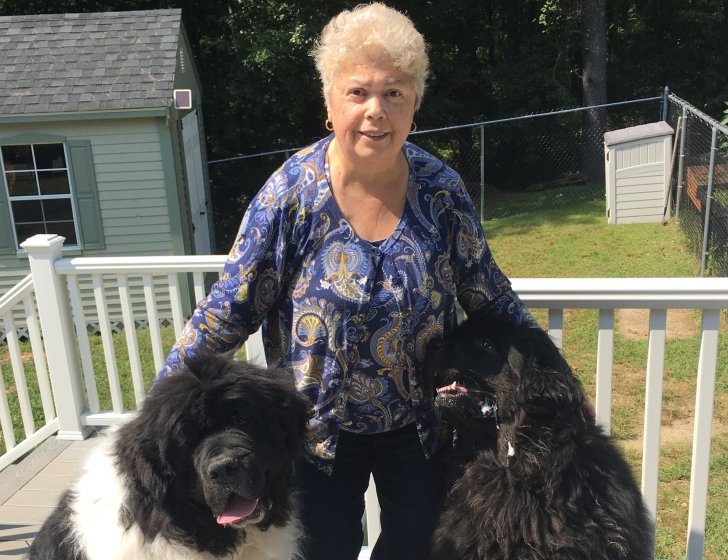 Barbara stands on a backyard porch, hugging two dogs