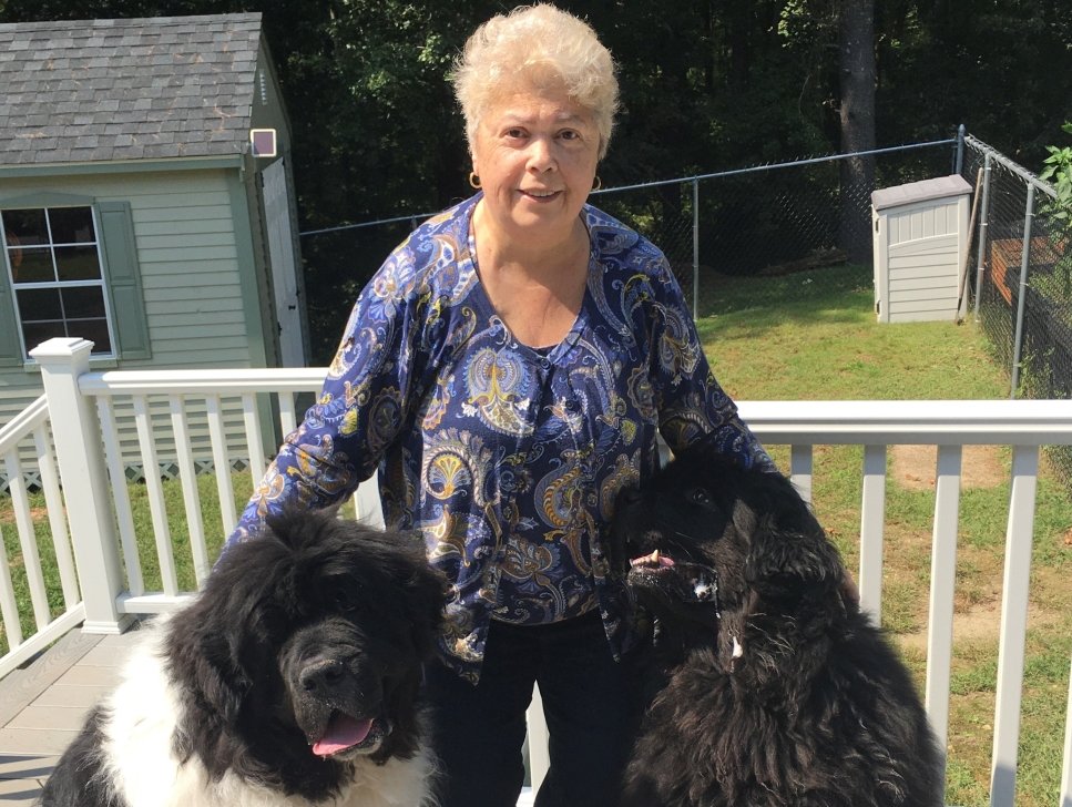 Barbara stands on a backyard porch, hugging two dogs