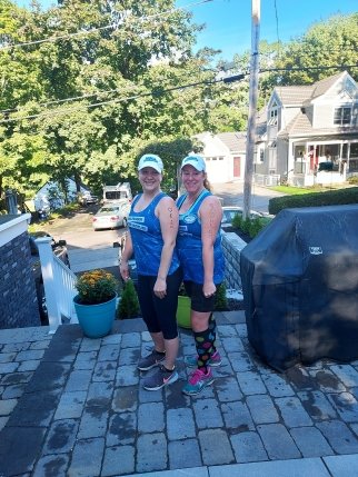 Sarah and teammate stand on a patio wearing their running singlets