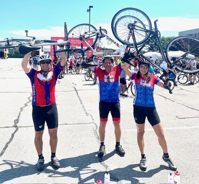 Three bikers stand together smiling and holding bikes above heads