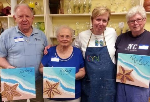 Cindy stands with three people holding up their paintings