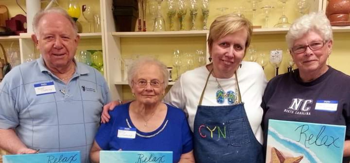 Cindy stands with three people holding up their paintings