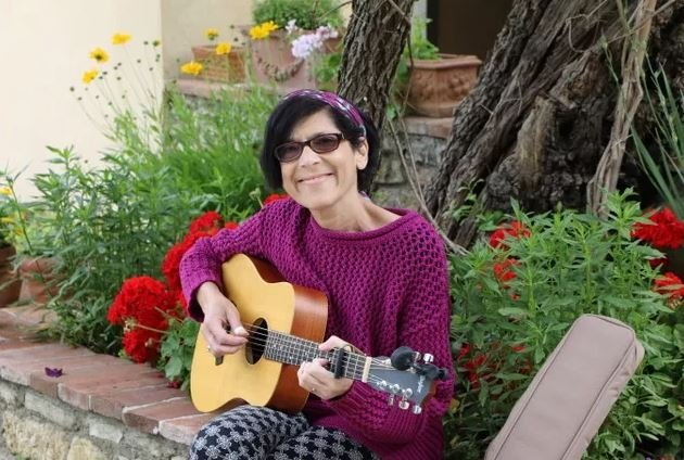 Patient sits on a stone wall playing guitar next to a garden