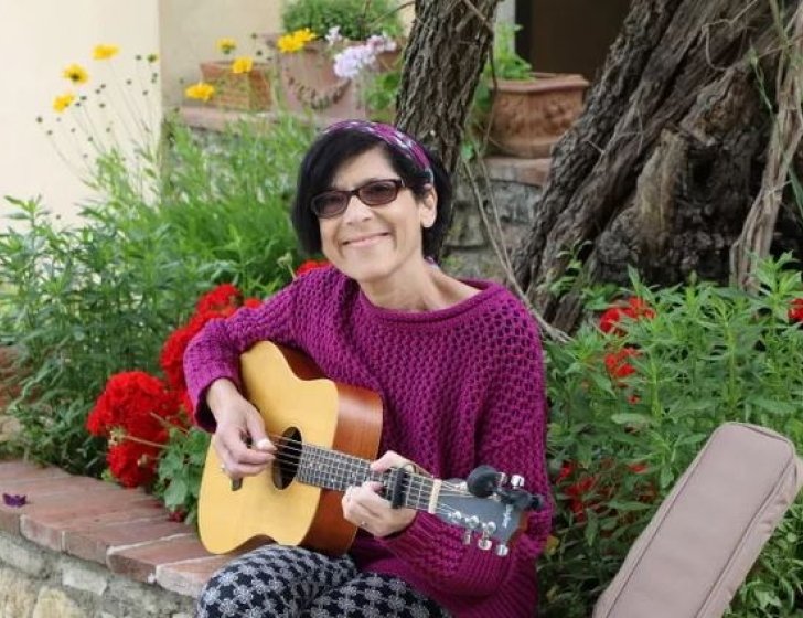 Patient sits on a stone wall playing guitar next to a garden