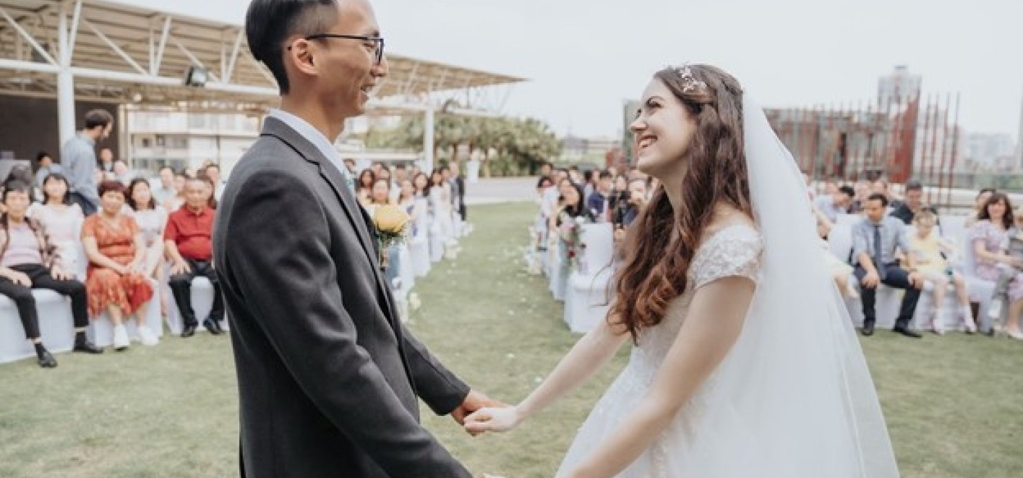 Husband and wife hold hands at wedding with family and friends watching