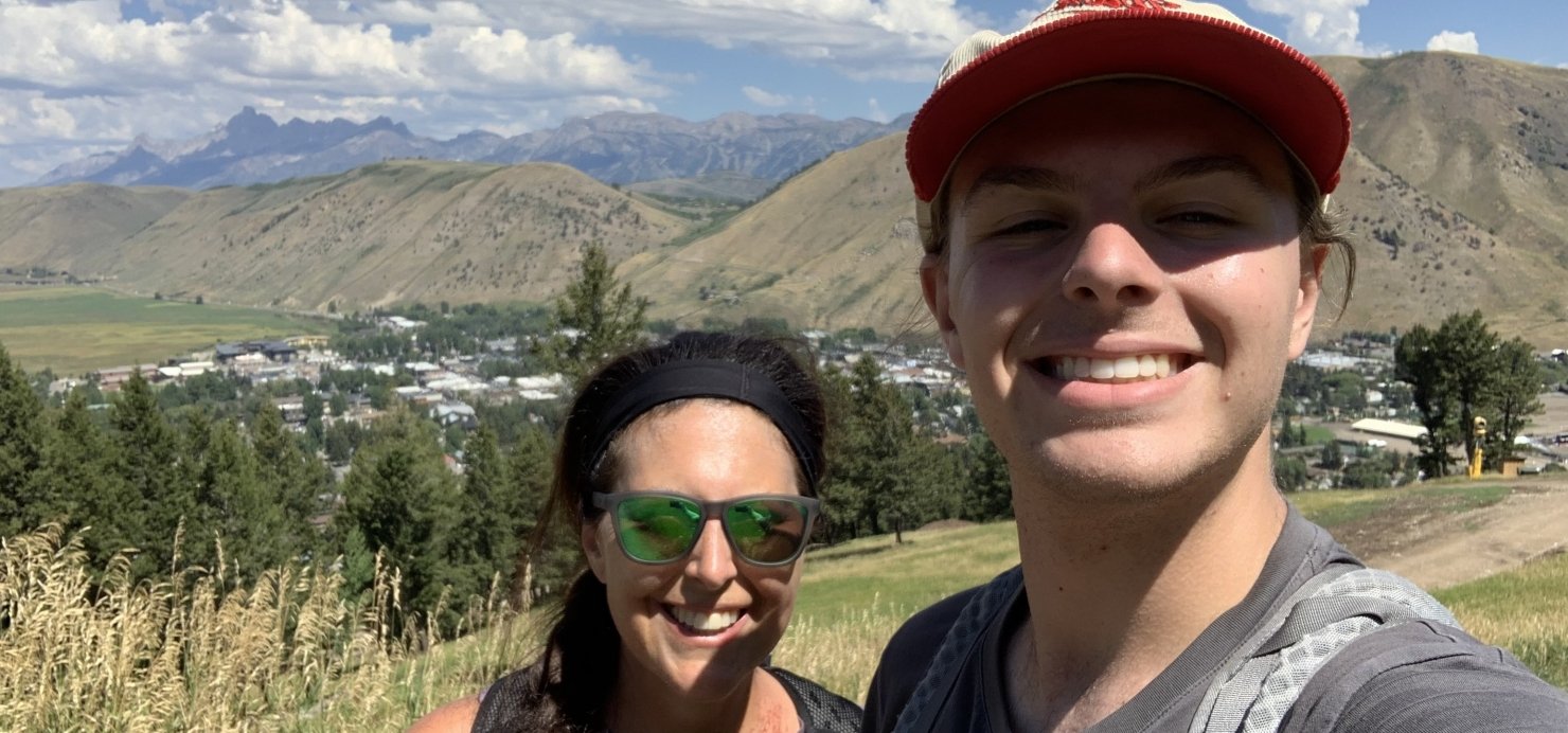 Marlene and son stand on a hiking trail with mountains in the background