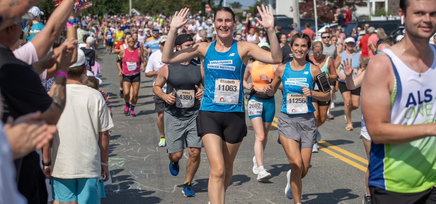 Elizabeth runs wearing a Dana-Farber singlet with arms in air