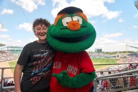 A teenager stands with Wally in front of a baseball stadium