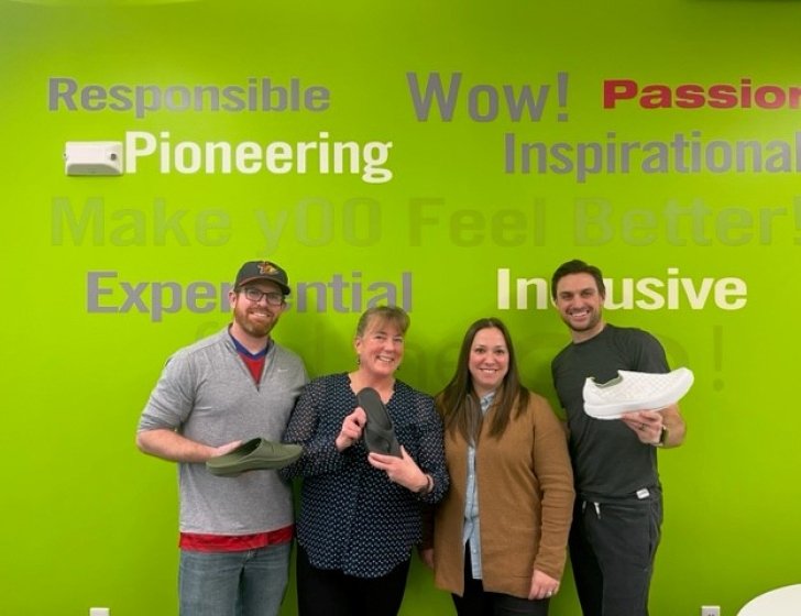 Suzanne with OOFOS staff at their office holding shoes