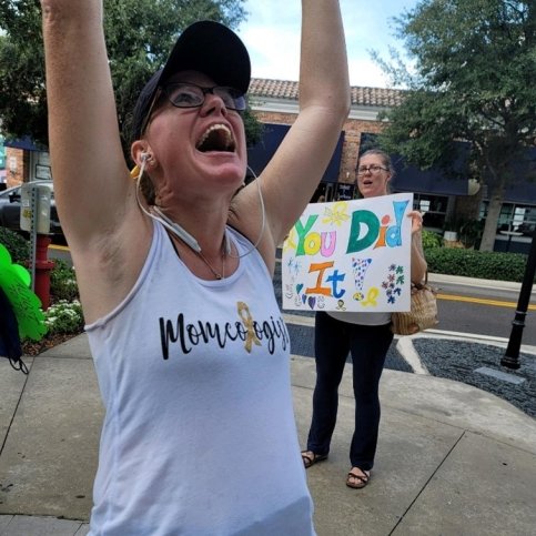 Christen wears running clothes and stands with arms in the air