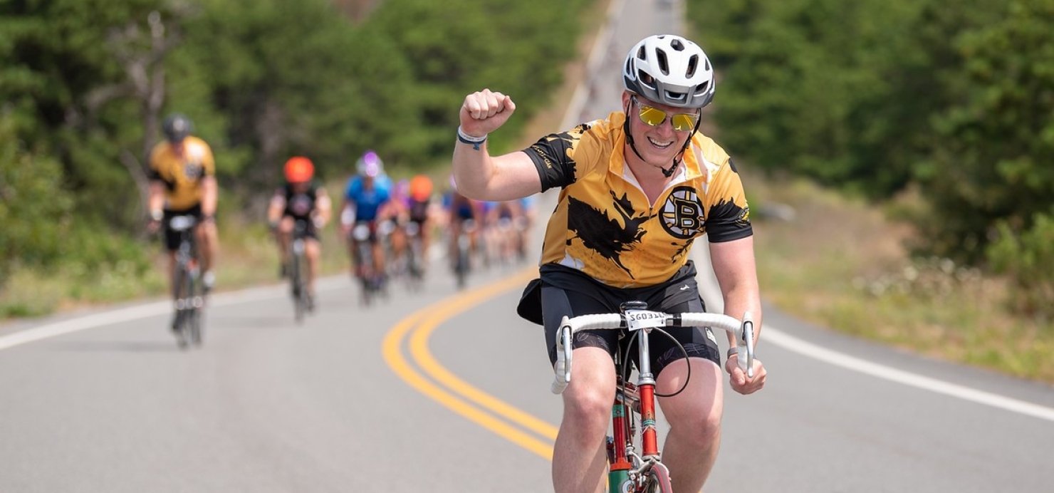 Sam rides a bike on a road with his fist in the air and other bikers behind him