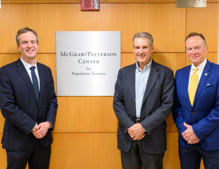 McGraw and Patterson families stand next to 'McGraw/Patterson Center for Population Sciences' wall sign