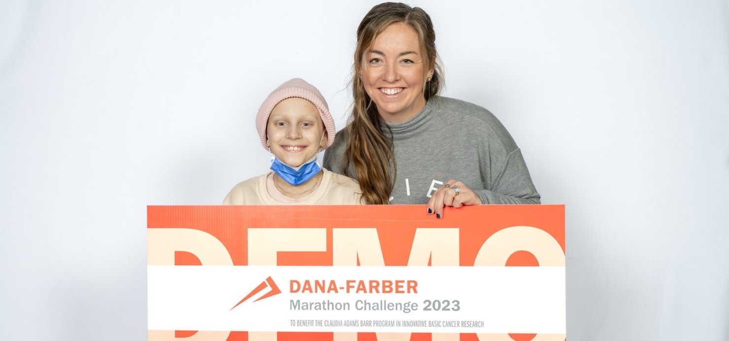 Sasha and Beth stand together holding a Dana-Farber Marathon Challenge 2023 sign