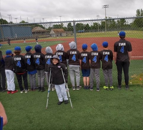 Evan on a baseball field using crutches with his teammates behind him