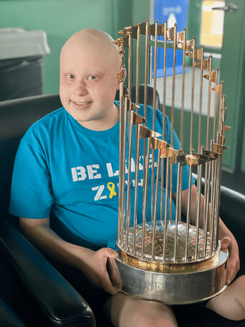 Zach sits in chair holding the World Series Championship trophy
