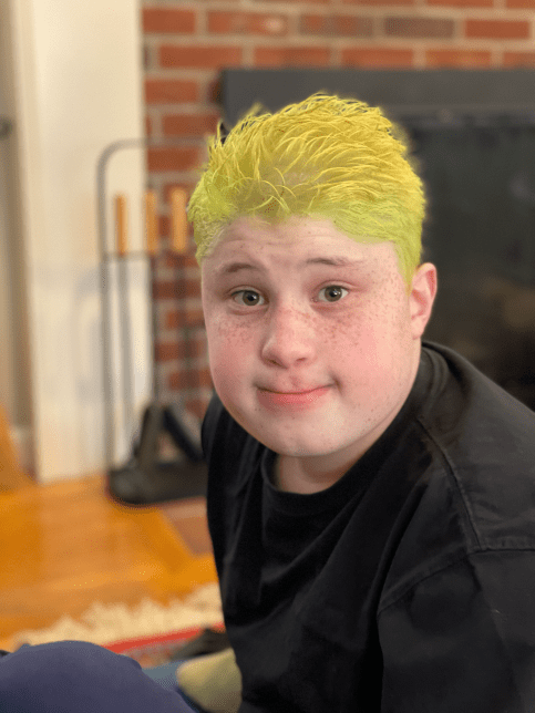 Zach sits on floor in living room, sporting green and yellow hair