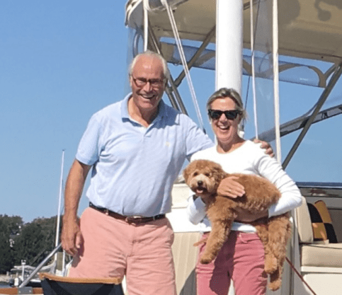 Candace and Larry stand on boat, holding a dog